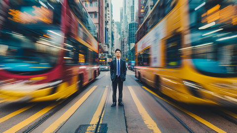 Portrait of a business person standing in the middle of the road, cars and busses are passing by with extreme motion blur. Busses and lines on the street are predominantly yellow. | © wob AG
