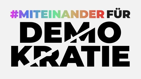 Only typography can be seen in the picture. At the top is "#Together" in colourful letters. The word "for" follows in black. Below it is "Democracy" in even larger letters. A light-coloured stripe runs through the word, which looks as if it is cutting the word "democracy" in half.