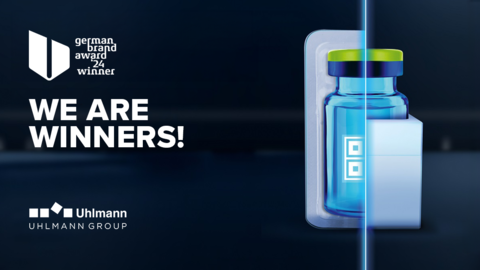 On a dark blue background, a parenteral is packaged on one side in a plastic tray and on the other side in a paper tray. A light blue strip of light runs down the centre, separating the two types of packaging and indicating where the two images have been combined. To the left is the signet of the German Brand Award for 2024, below which is the text "We are winners!" and below that the logo of Uhlmann Pac-Systeme.